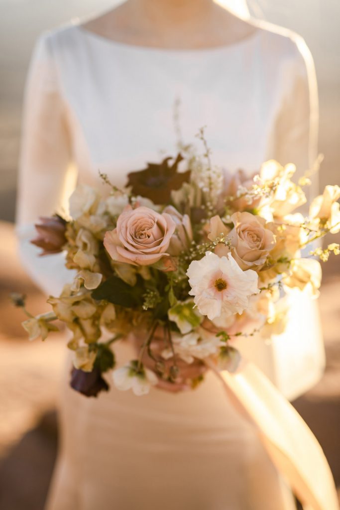 Bride showing her bouquet to the camera while she's surrounded by etheral sunlight.