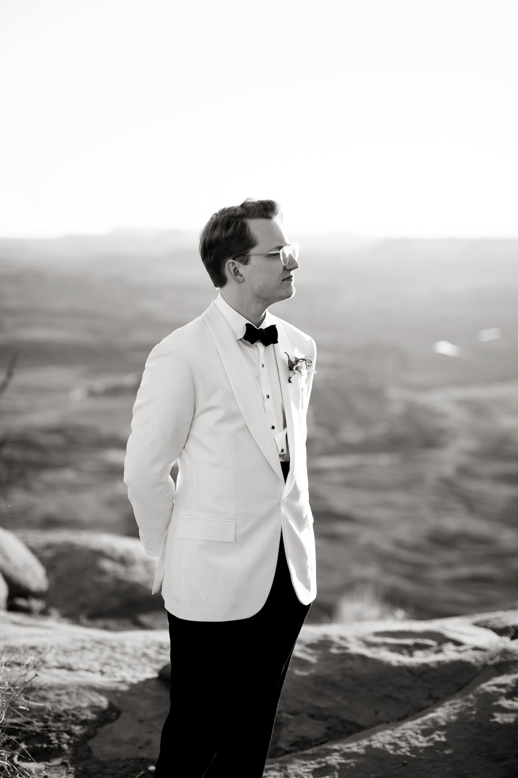 A portrait of a young groom wearing a white suit with a black bowtie.