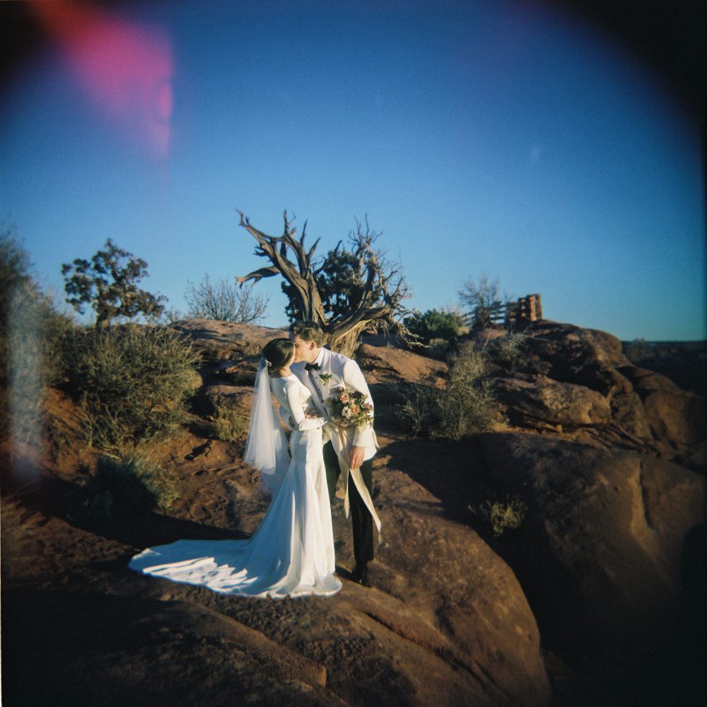 Holga film photo of a husband and wife wearing all white kissing in the Souther Utah desert.