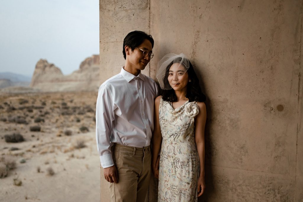 Wife wearing a small veil smiles at the camera while her husband looks lovingly at her.