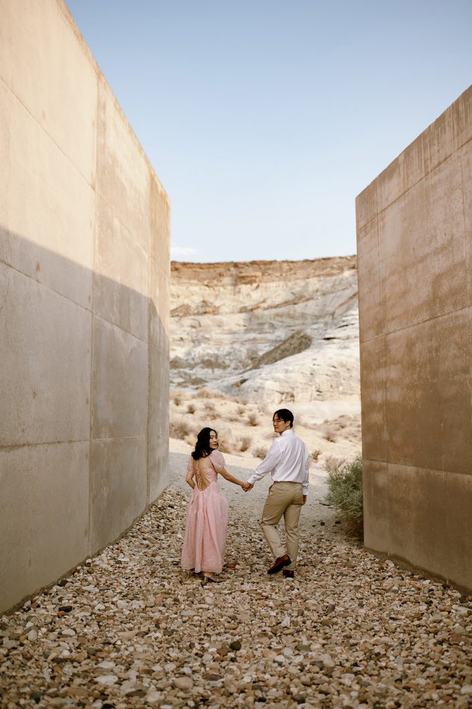 Couple walking away from the camera between two large modern cement walls.