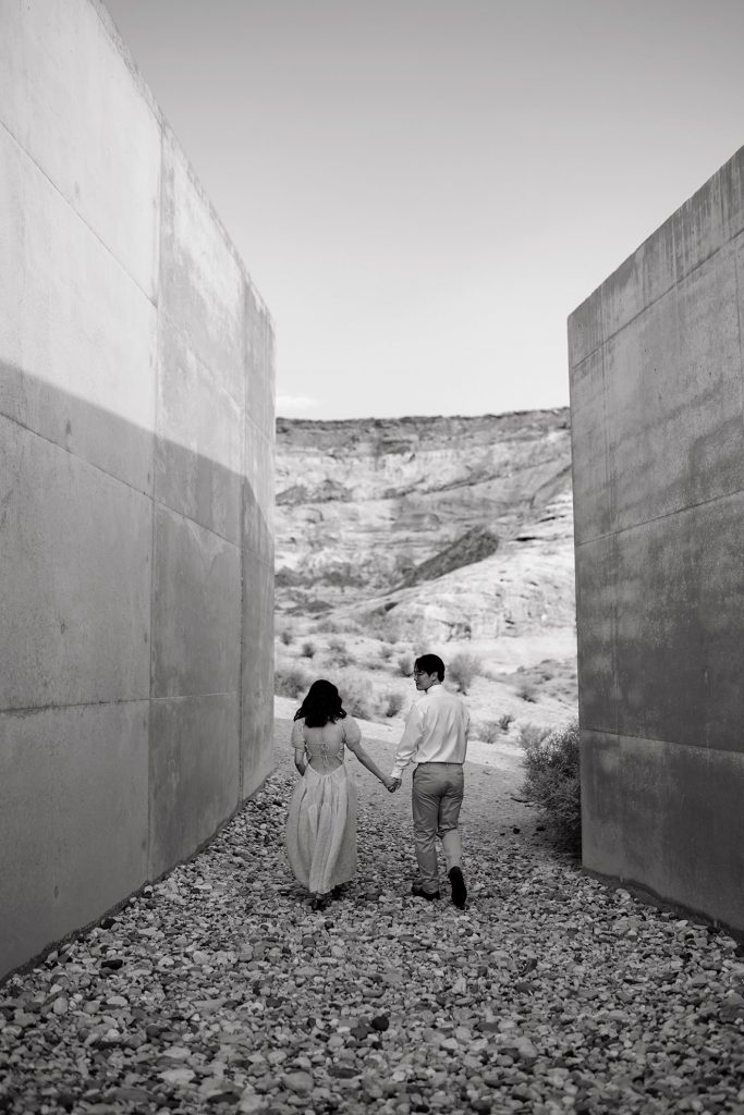 Black and white of couple walking on a rocky path between two large cement walls.