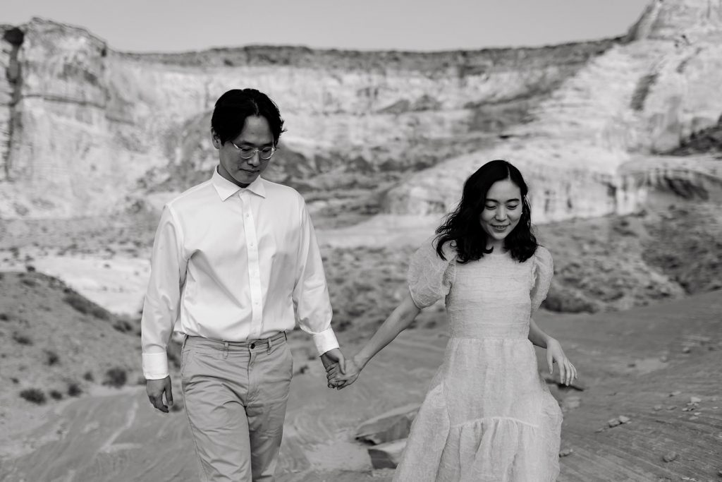 Husband and wife walk hand in hand with large desert bluffs in the backgorund.