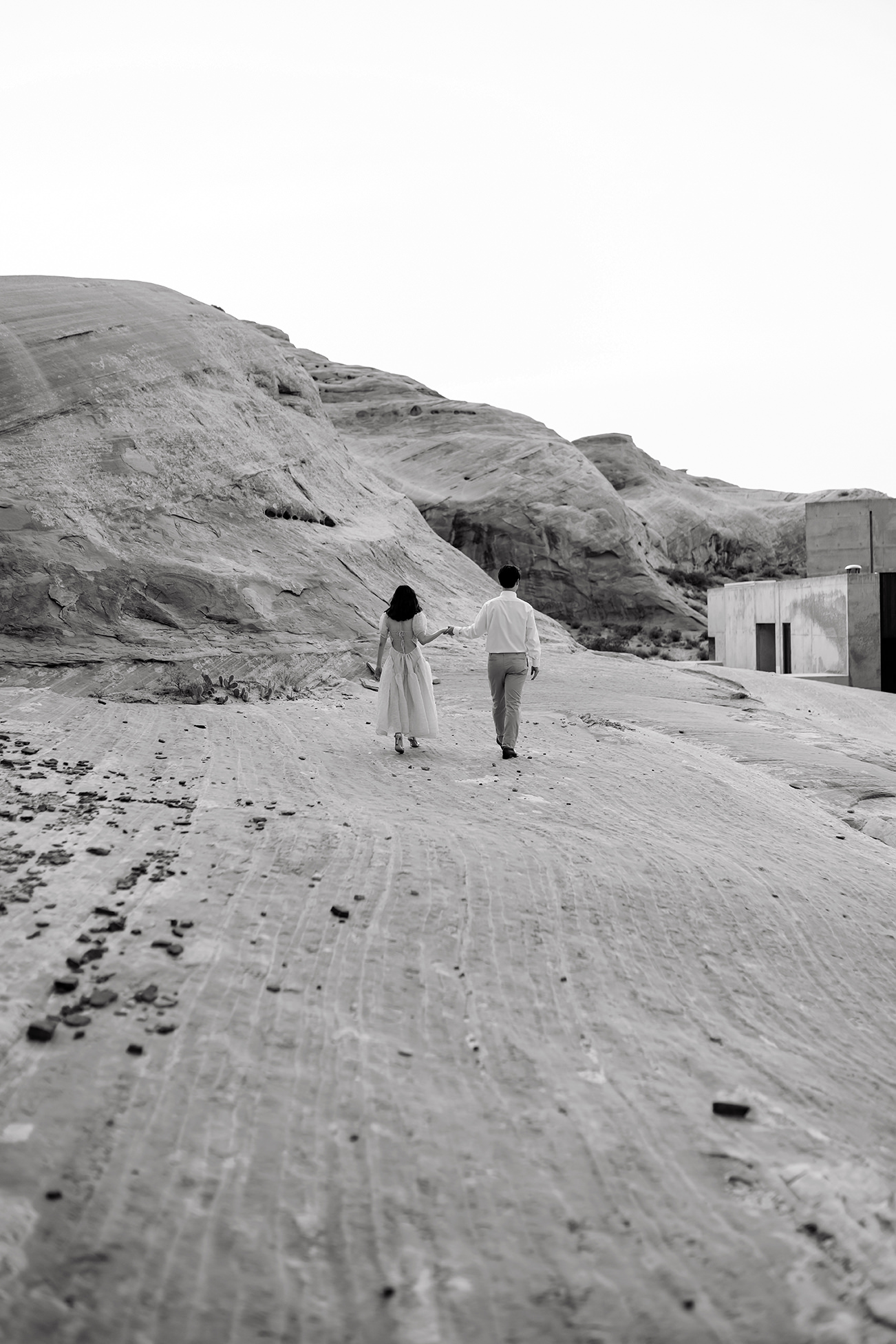 Black and white of the couple walking off back into the desert over the rocky ground.