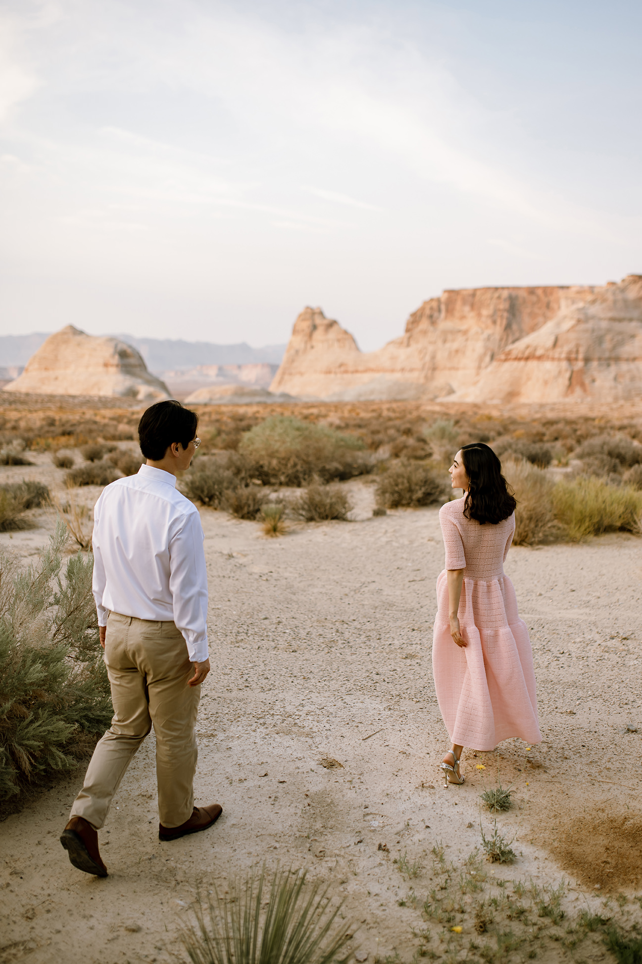 New wife in pink dress playfuly leads her husband through a small dessert clearing.