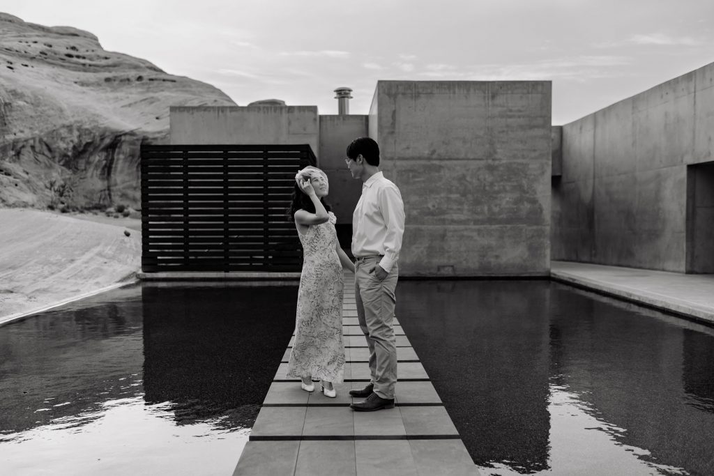 Bride fixes her veil while staring into her husband's eyes in black and white.