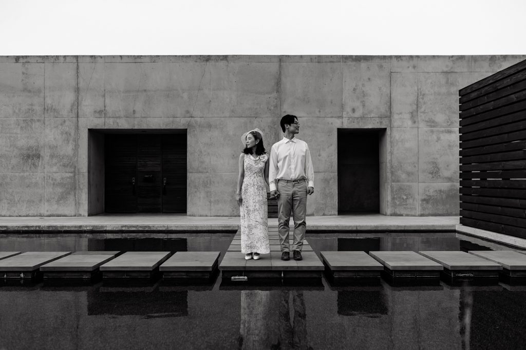 Couple pose facing away from each other on a watery path in black and white.