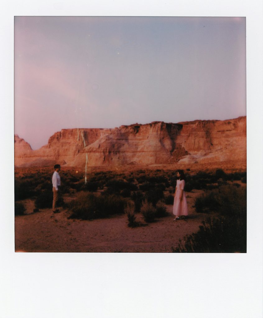 Poloroid of couple standing apart with the red Utah dessert plateus in the distance.