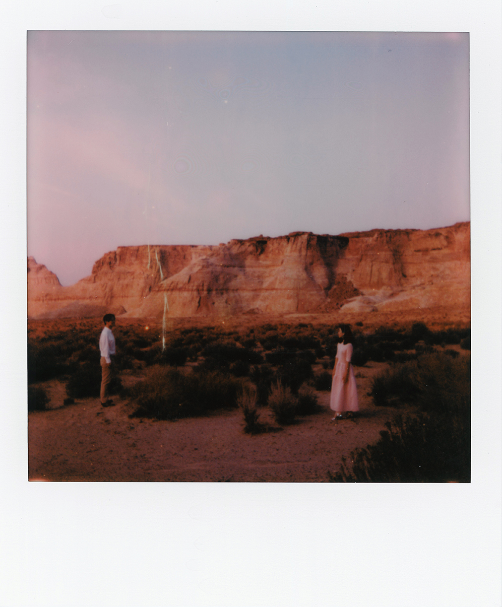 Poloroid of couple standing apart with the red Utah dessert plateus in the distance.
