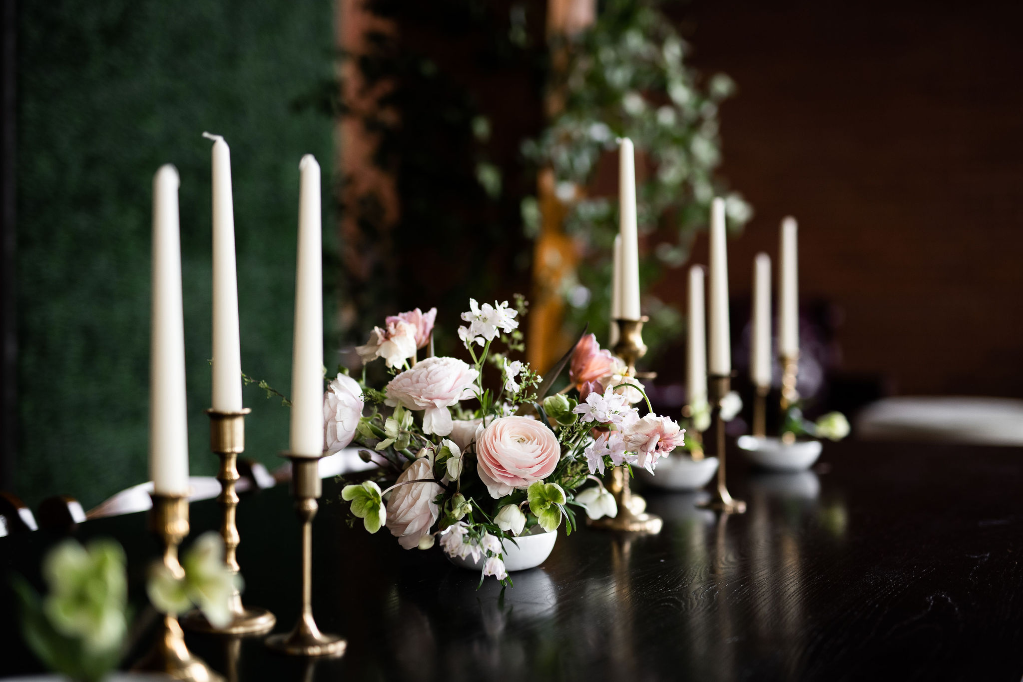 A beautiful flower arangment on a dark table surrounded by long candles.