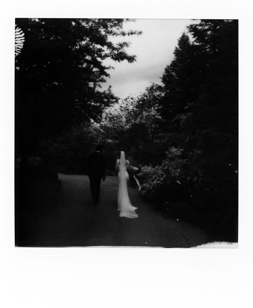 polaroid of a bride and groom walking through a garden